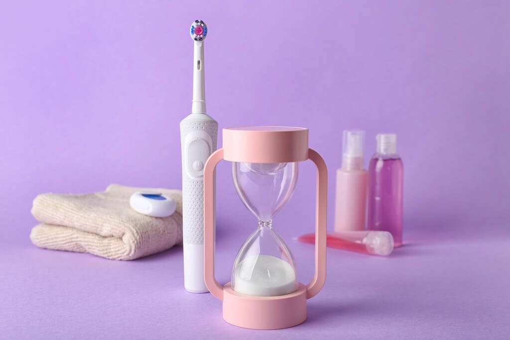 Hourglass and electric toothbrush on color background